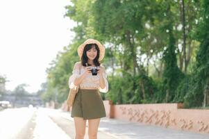 Portrait of asian young woman traveler with weaving hat and basket and a camera on green public park nature background. Journey trip lifestyle, world travel explorer or Asia summer tourism concept. photo