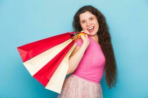 retrato de joven contento sonriente mujer con compras bolsas, terminado azul antecedentes. compra, rebaja y personas concepto foto