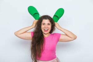 Pretty young woman fooling around with green slippers on white background photo