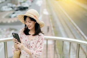 young asian woman traveler with weaving basket using mobile phone and standing on overpass with railway background. Journey trip lifestyle, world travel explorer or Asia summer tourism concept. photo