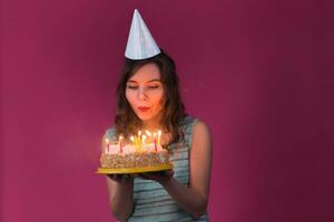 Portrait of pretty girl holding birthday cake and blowing candles at party photo