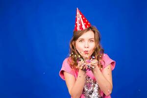 Close up portrait of attractive young woman blowing glitters. Caucasian Female model having fun over blue background. photo