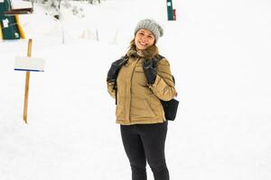mujer invierno senderismo. hermosa joven caucásico mujer disfrutando nieve vestido en un alegre invierno gorra y con un cartera en su espalda con espacio de copia. foto