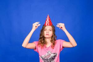 People, holidays, birthday and celebration concept - Woman in a festive cap dancing on the blue background photo