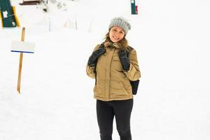 Woman winter hiking. Beautiful young caucasian woman enjoying snow dressed in a cheerful winter cap and with a satchel on her back with copyspace. photo