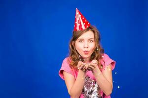 Portrait of beautiful woman blowing confetti in the air, party new years eve celebration on blue background photo