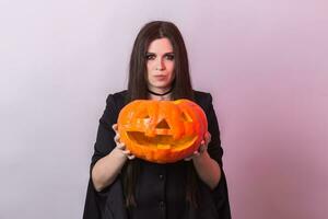 Young woman in Halloween witch costume in studio with yellow pumpkin. photo