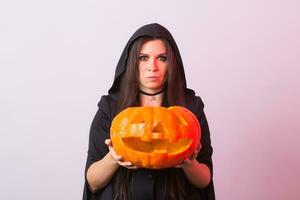 joven mujer en Víspera de Todos los Santos bruja disfraz en estudio con amarillo calabaza. foto