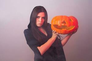 Gothic young woman in witch halloween costume with a carved pumpkin photo