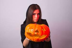 mujer como bruja es en pie con el calabaza en el estudio. Víspera de Todos los Santos y carnaval concepto foto