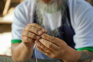 de cerca y cosecha manos de cuero artesano es cuidadosamente enhebrar un aguja a coser un cuero producto para un cliente. foto
