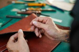 Closeup hand of leather craftsman is carefully to sew a leather bag for a customer., Leather craftsman concept. photo