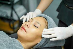 Cosmetologist use a cotton pad to clean on woman client face in beauty clinic. photo