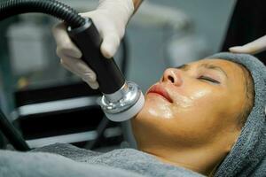 Closeup Asian beauty woman having therapy to stimulate facial skin and facial ultrasonic skincare treatment by professional cosmetologist wellbeing. photo