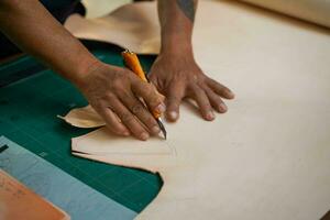 de cerca mano de cuero artesano es cuidadosamente utilizando un cortador cuchillo a cortar el blanco cuero. foto