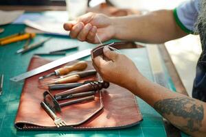 de cerca mano de cuero artesano es cuidadosamente a coser un cuero cinturón para un cliente., cuero artesano concepto. foto