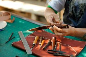 de cerca mano de cuero artesano es cuidadosamente a coser un cuero cinturón para un cliente., cuero artesano concepto. foto