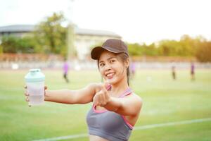 Young female relaxing after fitness training at the football stadium. She have a beautiful smile and acting make a hand mini heart for you photo