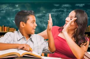 Latina School Teacher High Fiving a Young Hispanic Boy in the Classroom. photo