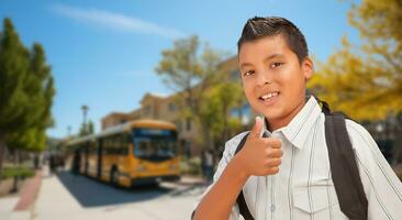 Excited Young Hispanic Boy Wearing a Backpack Giving a Thumbs Up on Campus photo