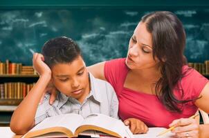 Female Tutor Doing Homework with a Young Hispanic Boy in the Classroom. photo