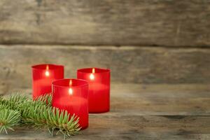 Three red candles and twig of spruce on wooden background photo