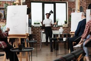 Art classes for adults. Group of different aged people attending drawing workshop, picking up new skills. Students sitting at easels in classroom and listening to instructor, learn to draw photo