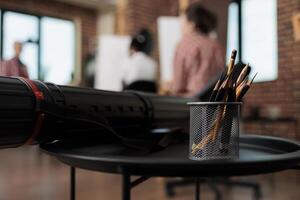 Pencils in metal holder and canvas tube on table in modern art studio, drawing tools and supplies in classroom. People learning to draw and sketch in group, fine arts education photo