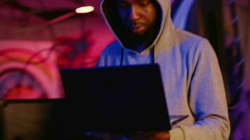 africano americano hacker dentro subterrâneo hq alvejando vulnerável sem patch conexões, tentando para pegue passado computador defesas e roubando valioso sensível dados, portátil Câmera tiro video
