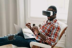 Relaxed man using VR headset with laptop, engaged in virtual experience. photo