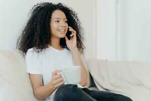 Smiling woman chatting on the phone and holding a mug, enjoying a relaxed moment at home photo