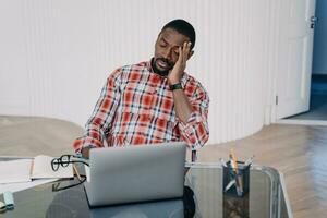 Stressed Black man at desk with laptop, feeling overwhelmed with work. photo