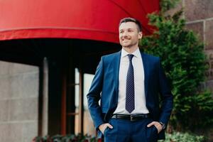 Confident businessman in a sharp suit smiling outside an upscale establishment with a red awning photo