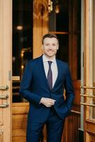 Smartly dressed man in a tailored blue suit and tie standing confidently in front of a luxury establishment photo