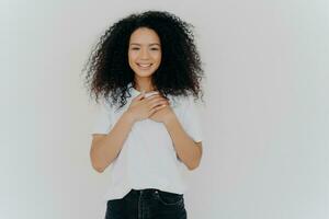 Grateful young lady with curly hair, hands on heart, expressing genuine thankfulness. photo