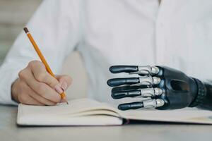 Focused individual writing in notebook with a mechanical prosthetic hand, showcasing adaptive technology photo