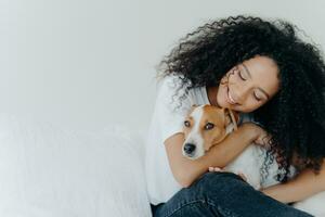 sereno mujer con Rizado pelo cariñosamente abrazando su perro, compartiendo un pacífico momento foto