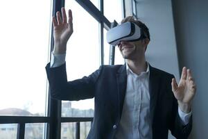 Smiling man in suit with VR headset, gesturing with raised hands photo