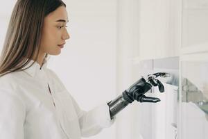 Focused woman using a sophisticated bionic hand to interact with a touchscreen, blending daily life with modern tech photo