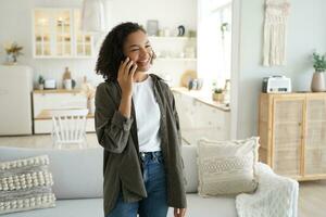 Smiling Black woman chatting on phone in a stylish, cozy living room photo