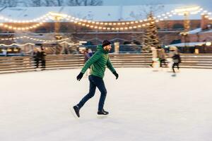 Focused man gliding on an ice rink with holiday lights and a Christmas tree. photo