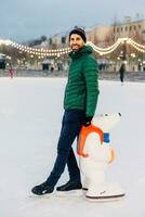 Smiling man ice-skating with a polar bear figure in a city rink under twinkling lights photo