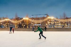 Man in green jacket enjoying ice skating on a rink with city lights at dusk photo