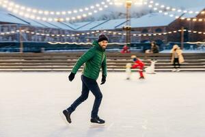 Man ice-skating joyfully in an outdoor rink with festive lights at twilight photo