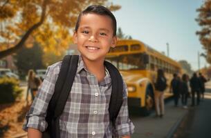 linda joven Hispano chico vistiendo un mochila cerca un colegio autobús en instalaciones. foto
