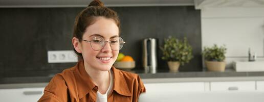 Vertical shot of woman working from home, business owner using laptop, browsing social media on computer, wearing glasses photo