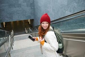 Smiling girl walking on stairs, using mobile phone, texting message on her way, using smartphone app map, follows route to destination place photo