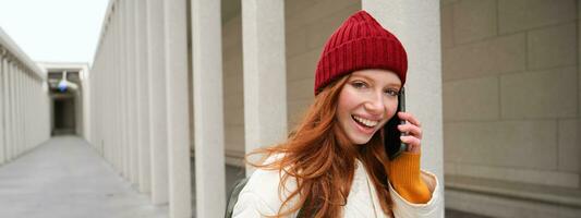 Happy redhead woman, girl with phone talks, has conversation on mobile app, uses internet to call abroad with smartphone app, laughing and smiling photo