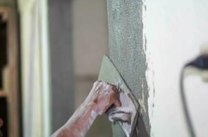 Closeup hands of builder holding mortar pan and plastering walls with cement in construction site. photo