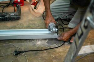 de cerca manos de el Maestro Sierra el metal participación eléctrico ángulo amoladora trabajando corte aluminio Tablas de madera a construcción sitio. foto